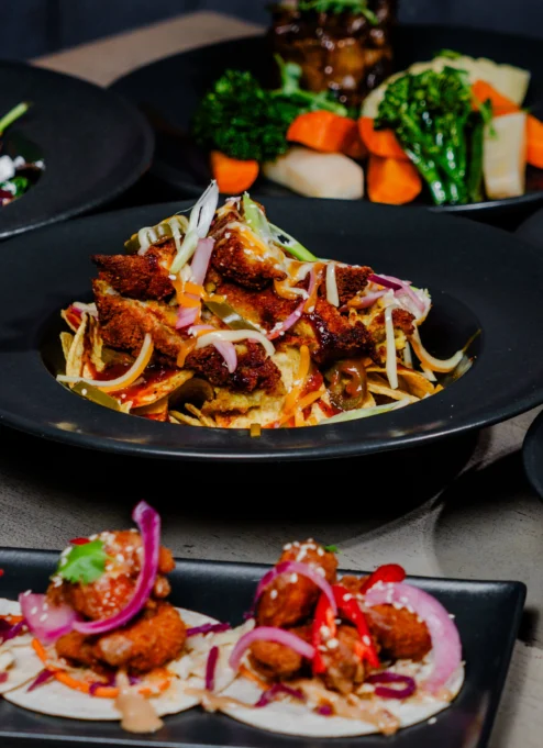 A variety of gourmet dishes served on black plates, showcasing colourful, fresh ingredients.
