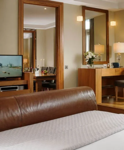 Elegant hotel suite with a large bed, modern decor, and cityscape view from the window.