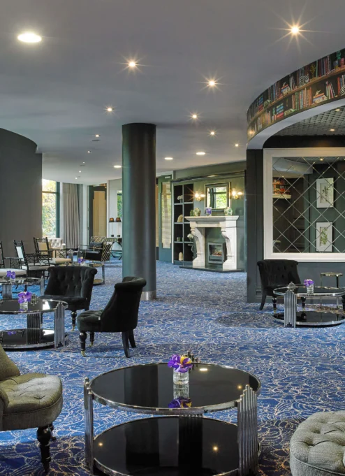 Cosy hotel lounge with comfy seating and bookshelf wallpaper, inviting for families to relax.