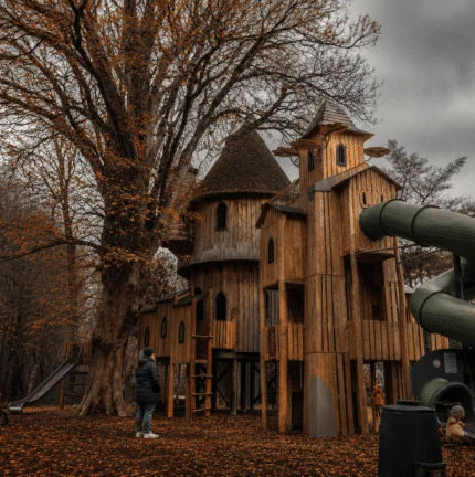 Family exploring a whimsical wooden treehouse in an autumn park setting.