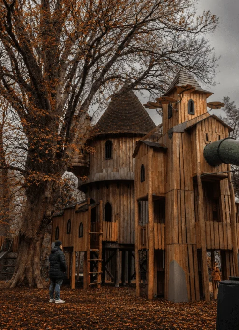Family exploring a whimsical wooden treehouse in an autumn park setting.