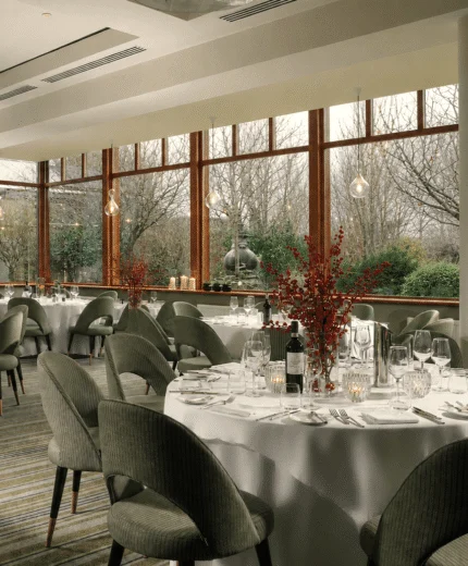 Elegant dining room with round tables set for dinner, overlooking a garden view.