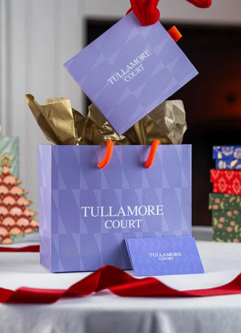 Festive Tullamore Court Hotel gift bag with Christmas decorations on a table.