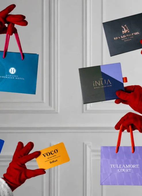 Festive hands holding gift cards for Tullamore Court Hotel and more, against a white panelled background.