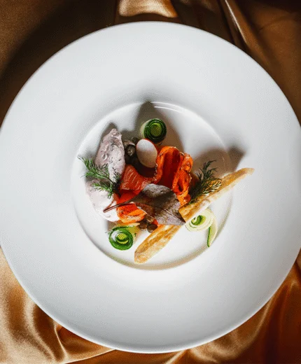 Elegant gourmet dish on a white plate with rich, golden fabric backdrop.